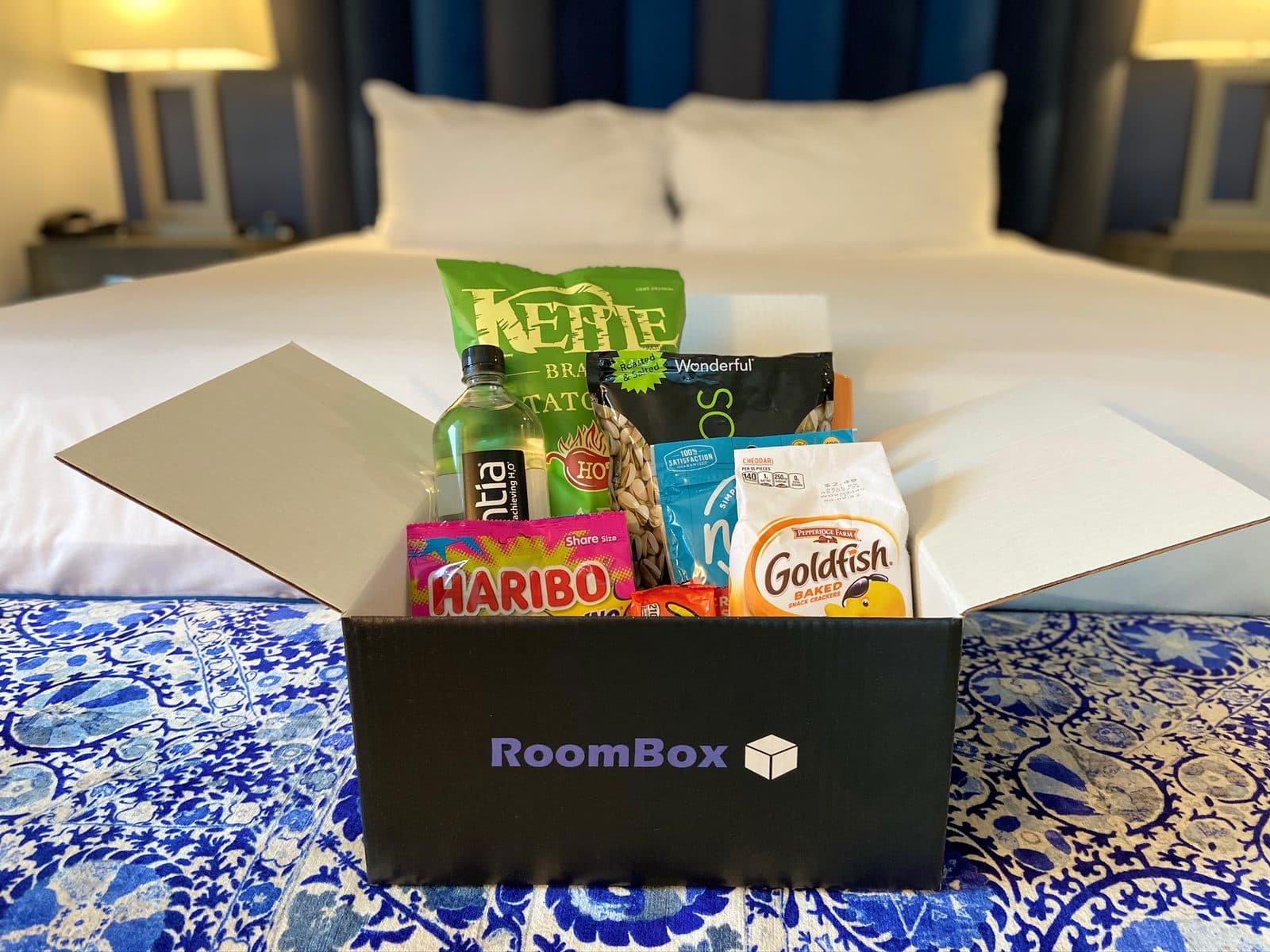 A RoomBox box of snacks and drinks waiting on a hotel bed